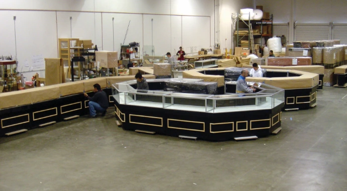 Glass jewelry showcases with black bases and gold-toned trim arranged in an island configuration during assembly in a workshop.